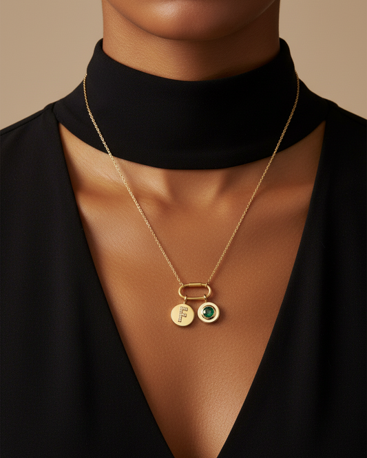 Gold necklace with a round pendant featuring the letter 'F' and a green gemstone on a white background.